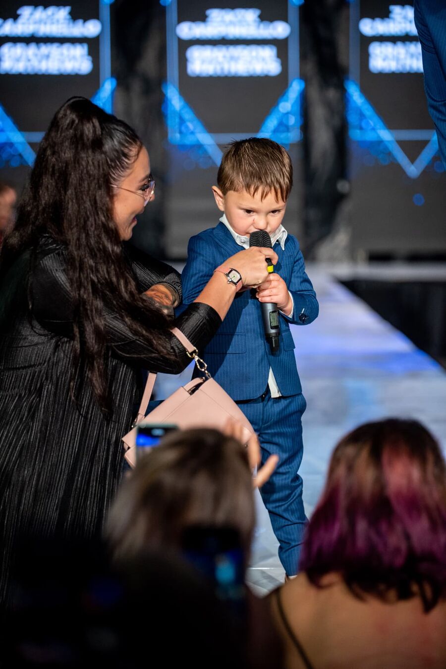 A mentor helping a young boy speak into a microphone at a David Alan Dreams event